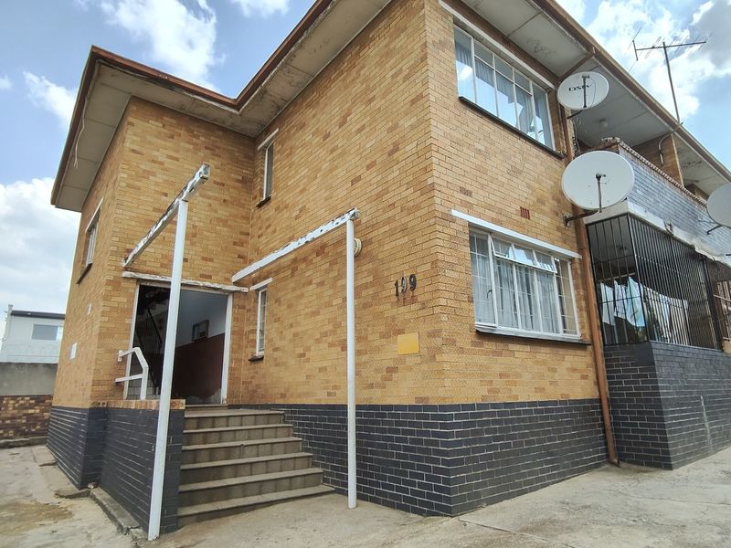 Exterior view of a multi-story apartment building featuring a face brick facade, security bars, and concrete entrance stairs.