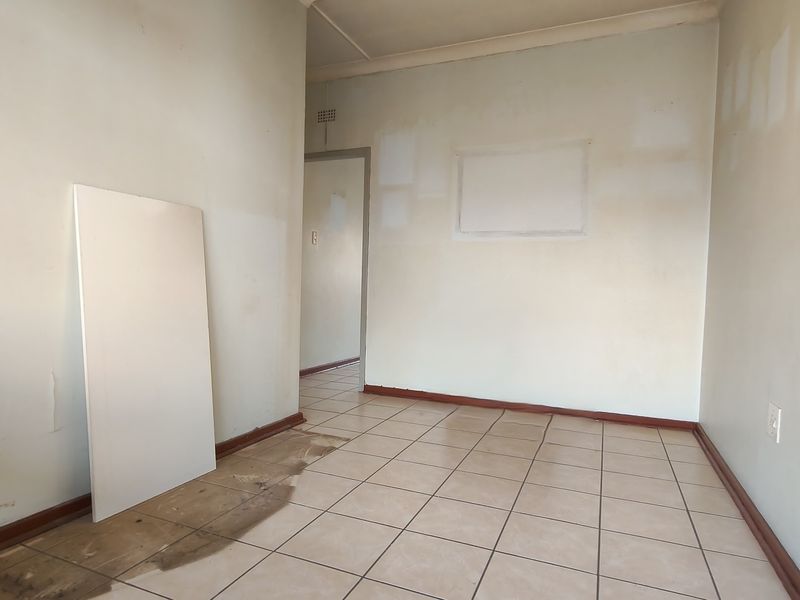 An empty living area featuring tiled flooring and neutral walls, currently requiring cosmetic updates and repairs to the floor and wall finishes.