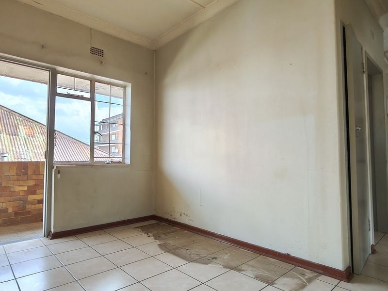 An empty living area featuring tiled flooring, a sliding door leading to a balcony, and visible signs of wear on the walls and floor.