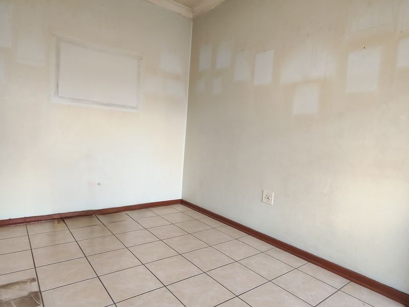 An empty bedroom featuring tiled flooring and walls requiring repainting, offering a blank canvas for renovation and personalization.
