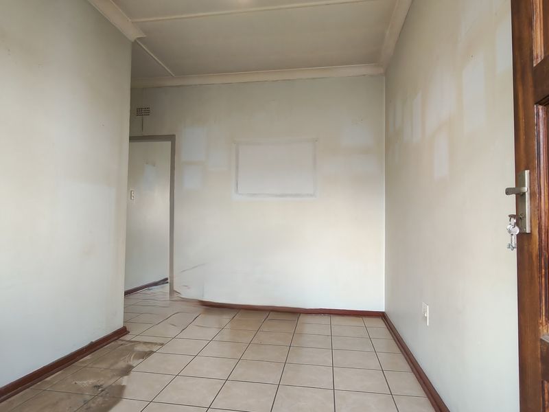 An empty living area featuring ceramic floor tiles and a timber door, currently requiring cosmetic wall repairs and floor maintenance.