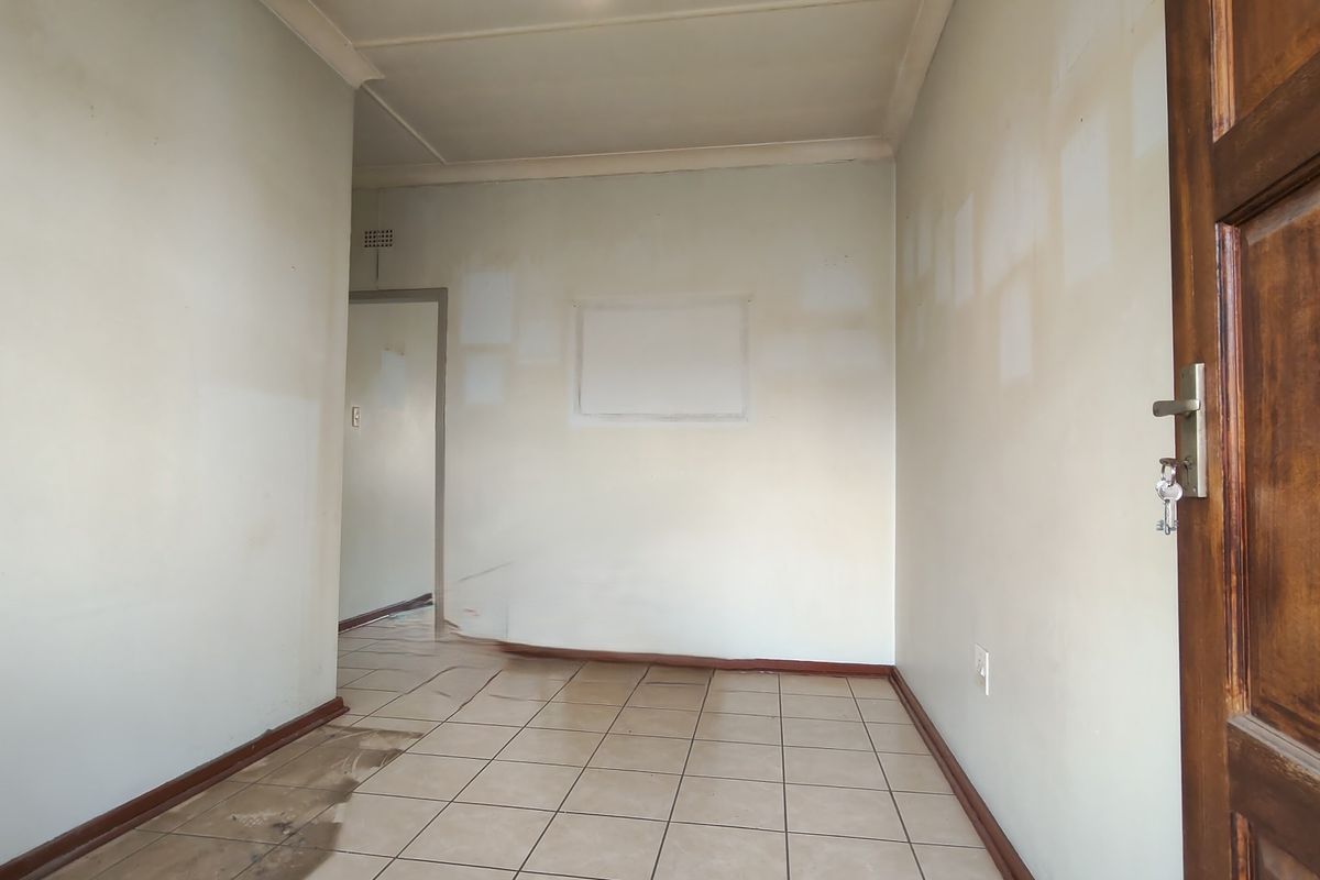 An empty living area featuring ceramic floor tiles and a timber door, currently requiring cosmetic wall repairs and floor maintenance.