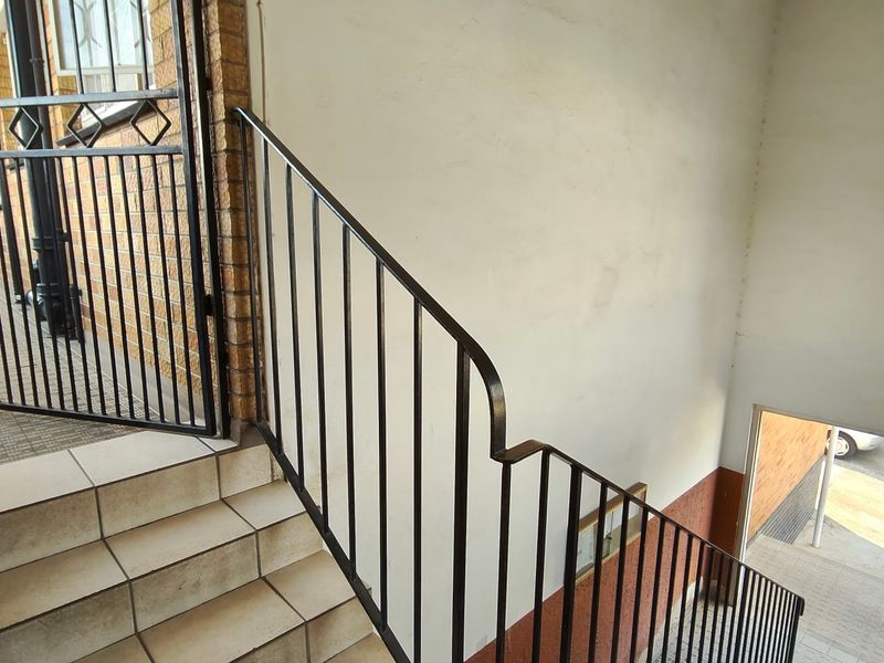 A communal apartment hallway featuring a metal security gate, tiled staircase, and metal balustrade leading to the building entrance.