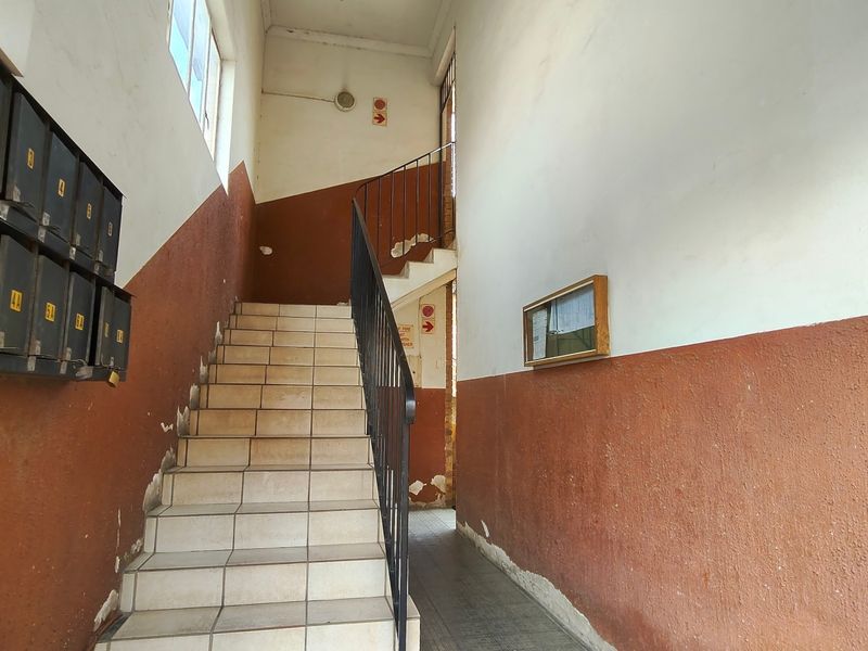 Communal apartment building hallway featuring a tiled staircase, metal handrail, and wall-mounted mailboxes, showing signs of wear and requiring maintenance.