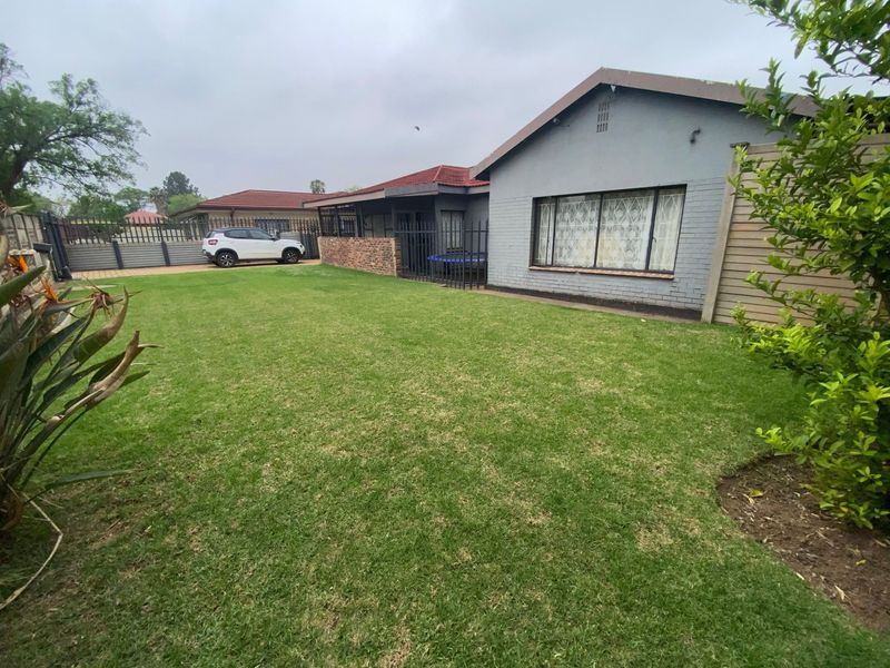 A spacious rear garden featuring a well-maintained lawn, enclosed by metal security fencing and brick boundary walls, adjacent to the main house structure.