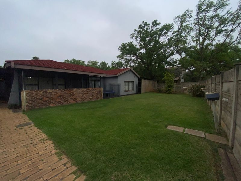 A spacious rear garden featuring a lawn, paved walkway, and a covered patio area, enclosed by brick and precast boundary walls.