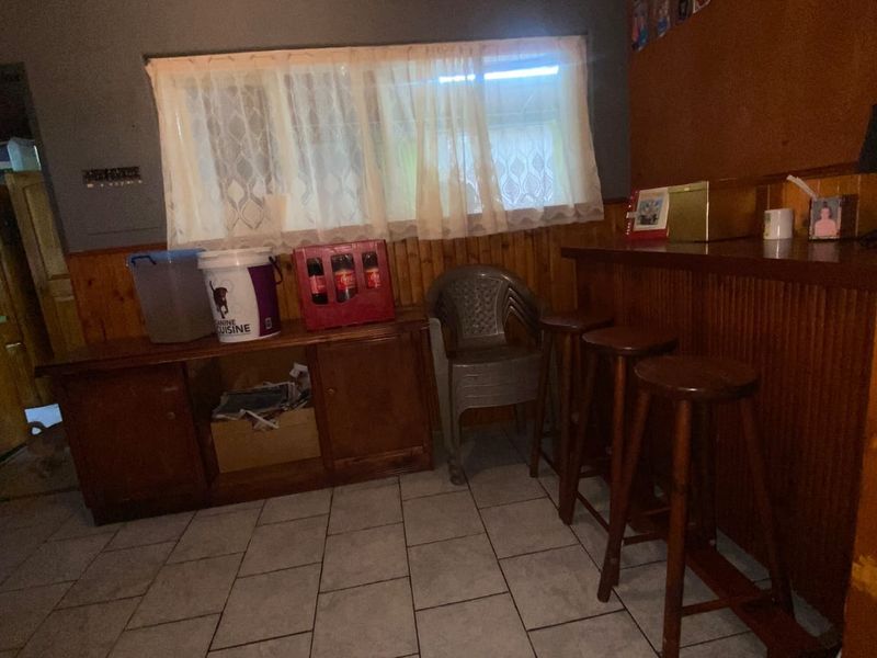 A dedicated bar area featuring a built-in wooden counter, tiled flooring, and wood-paneled walls, offering potential for a modern entertainment space update.