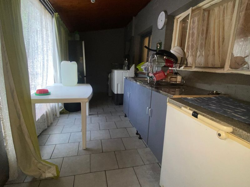 A functional scullery area featuring tiled flooring, built-in cabinetry with a sink, and a timber-paneled ceiling.