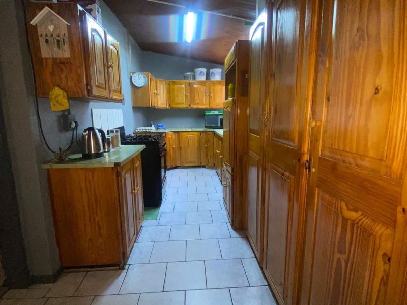 A narrow kitchen featuring extensive wooden cabinetry, tiled flooring, and a functional layout with built-in cooking appliances.
