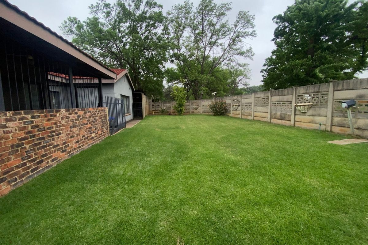 A spacious rear garden featuring a well-maintained lawn, enclosed by a precast concrete boundary wall and a face brick wall.