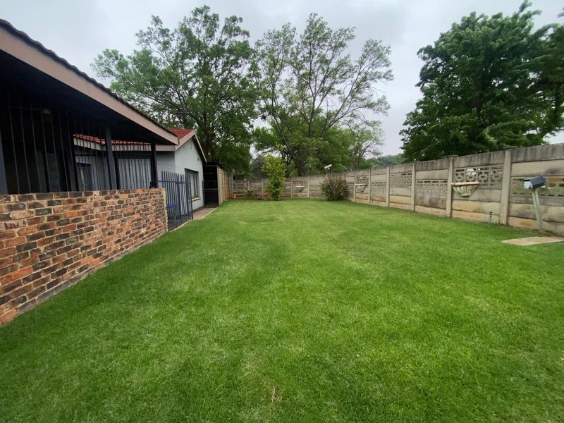 A spacious rear garden featuring a well-maintained lawn, enclosed by a precast concrete boundary wall and a face brick wall.