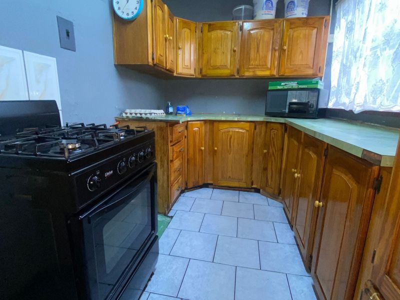 A functional kitchen featuring wooden cabinetry, a gas stove, and tiled flooring, offering a dated aesthetic with potential for modernization.