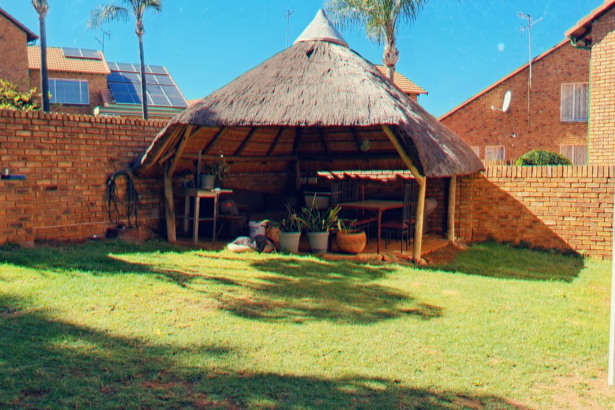 A rear garden area featuring a traditional thatched lapa and a built-in brick braai, set within a private walled yard.