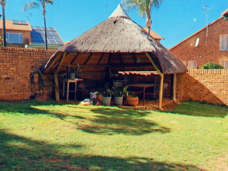 A rear garden area featuring a traditional thatched lapa and a built-in brick braai, set within a private walled yard.
