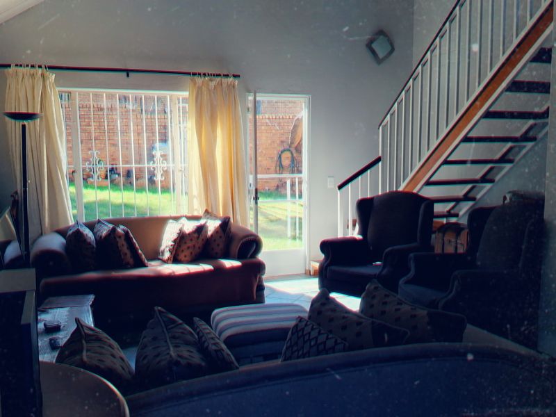 A living room featuring a staircase, security gate, and large windows with security bars, providing access to the rear garden area.