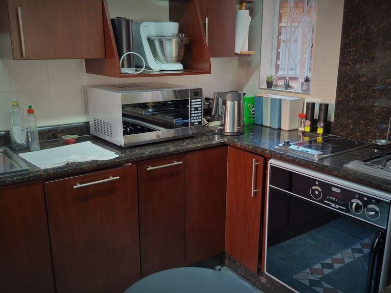 A functional kitchen featuring dark wood cabinetry, granite countertops, a built-in oven, and an electric hob with a tiled backsplash.