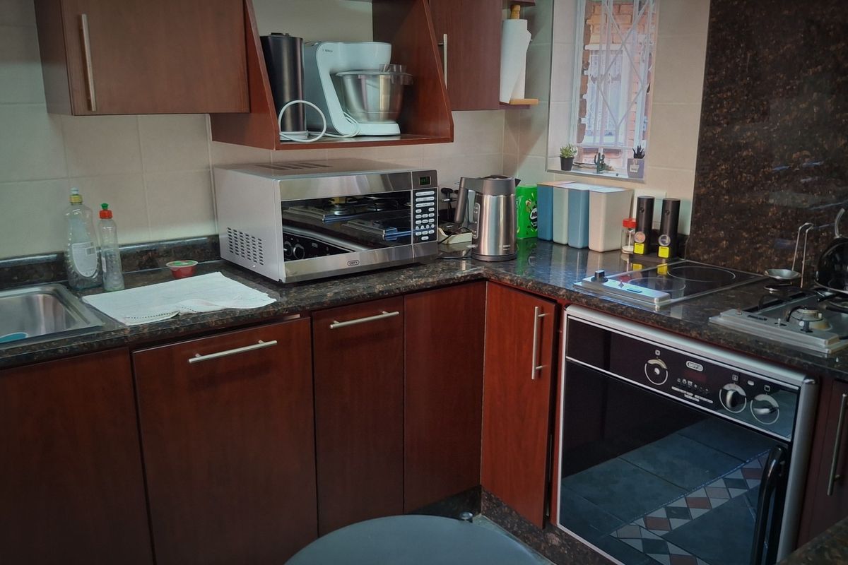 A functional kitchen featuring dark wood cabinetry, granite countertops, a built-in oven, and an electric hob with a tiled backsplash.