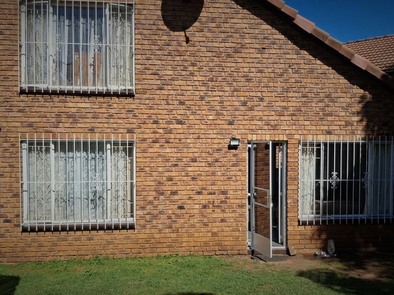 Rear elevation of a double-story face brick cluster home featuring security bars on windows and a tiled roof.
