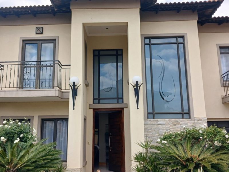 A well-maintained double-storey residential facade featuring decorative glass windows, wrought iron balcony railings, and stone cladding accents at the main entrance.