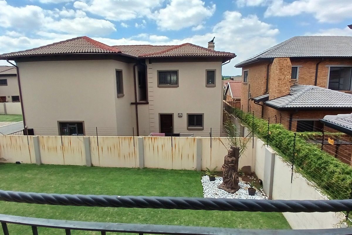 Rear view of a two-story house featuring a private garden, lawn area, and perimeter wall with electric fencing.