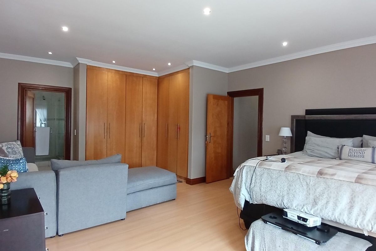 Spacious bedroom featuring built-in wooden cupboards, laminate flooring, recessed downlights, and direct access to an en-suite bathroom.