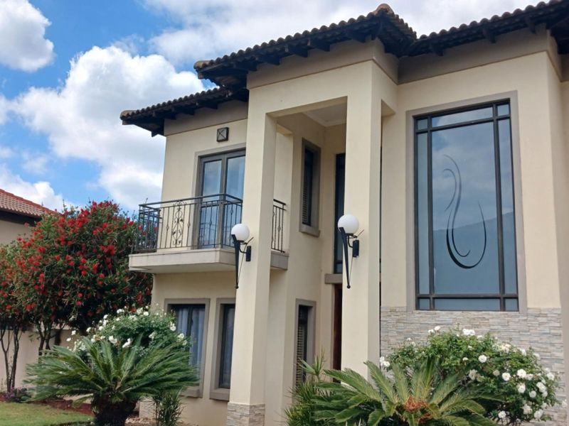A well-maintained double-storey residential facade featuring terracotta roof tiles, stone cladding accents, and a decorative wrought iron balcony.