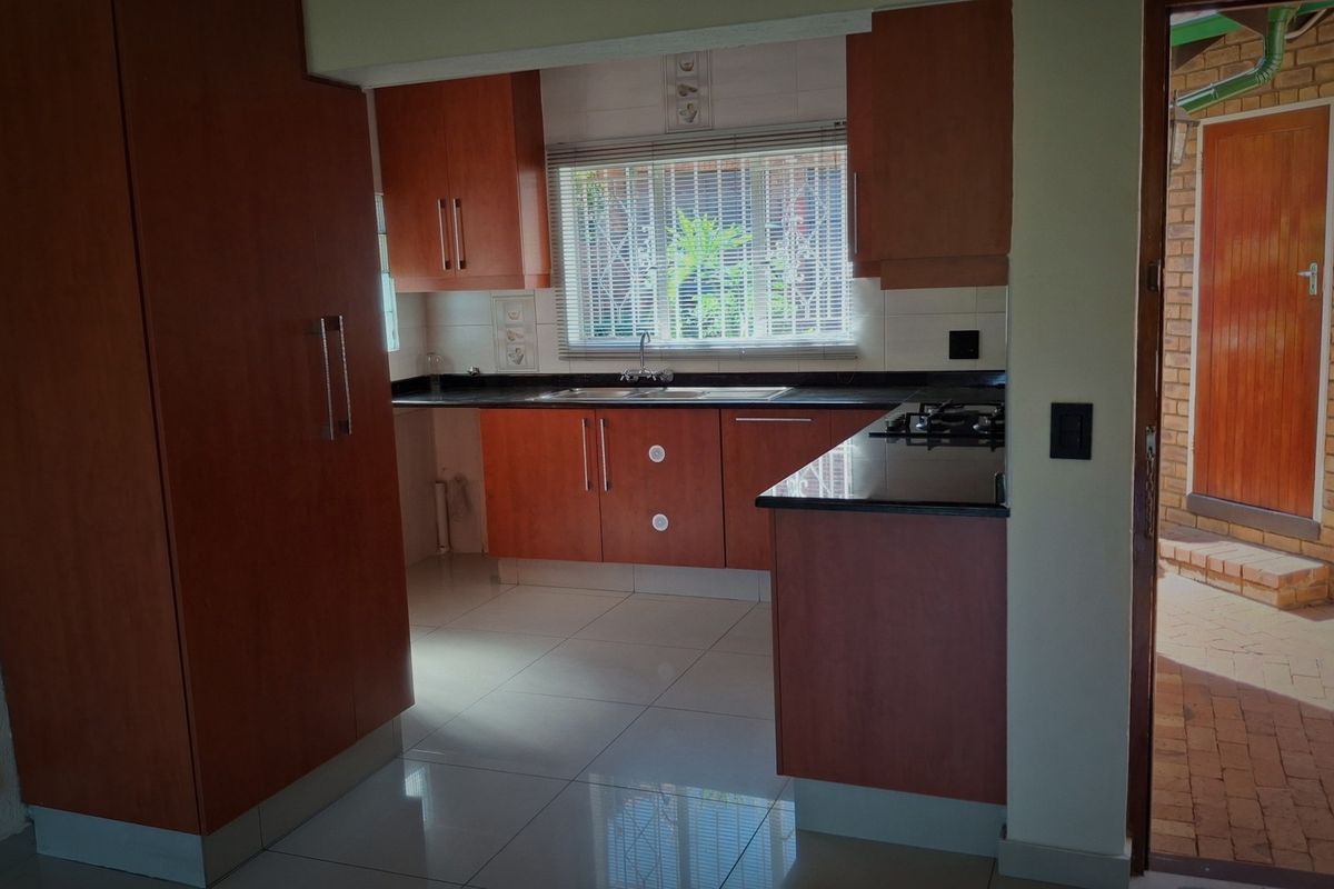 A functional kitchen featuring wood-finish cabinetry, granite countertops, a gas hob, and tiled flooring, with direct access to an outdoor patio area.