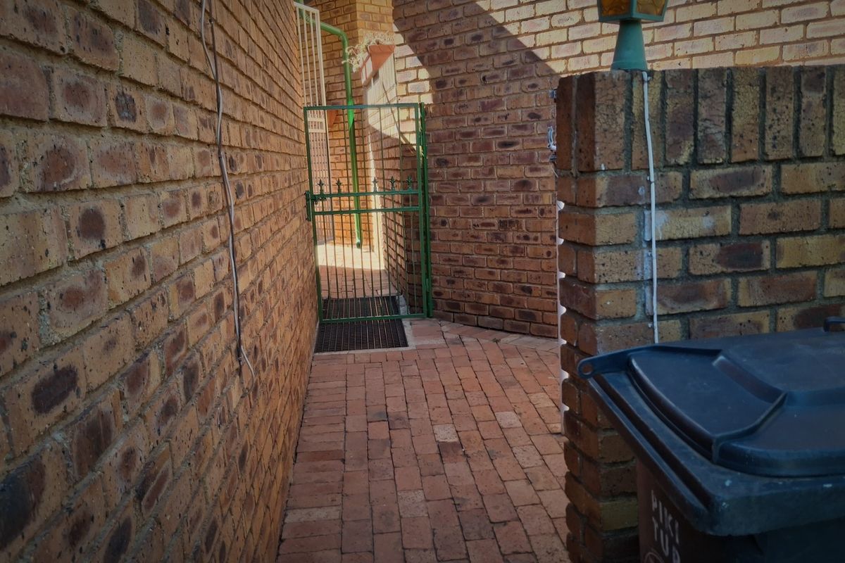 A narrow side passage featuring facebrick walls, brick paving, and a secure metal gate leading to the rear area.