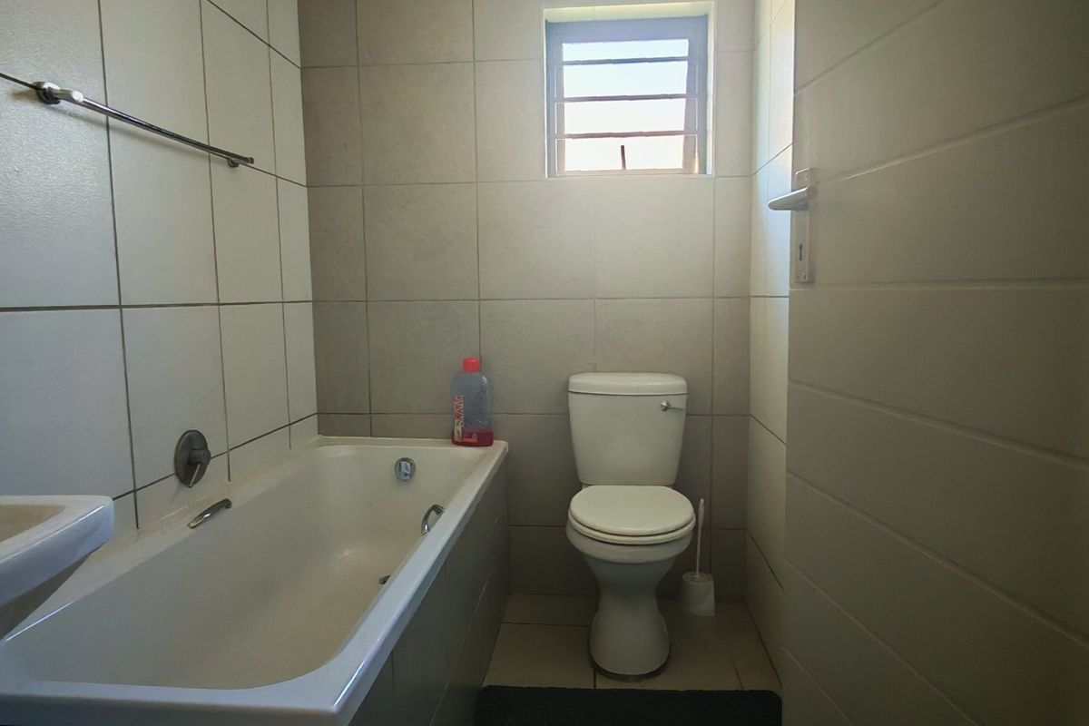 A functional bathroom featuring a bathtub, toilet, and neutral wall tiling, providing a clean and practical space.