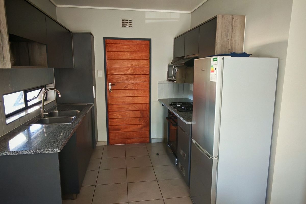 Modern galley-style kitchen featuring dark cabinetry, granite countertops, tiled flooring, and integrated appliances, providing a functional and contemporary cooking space.