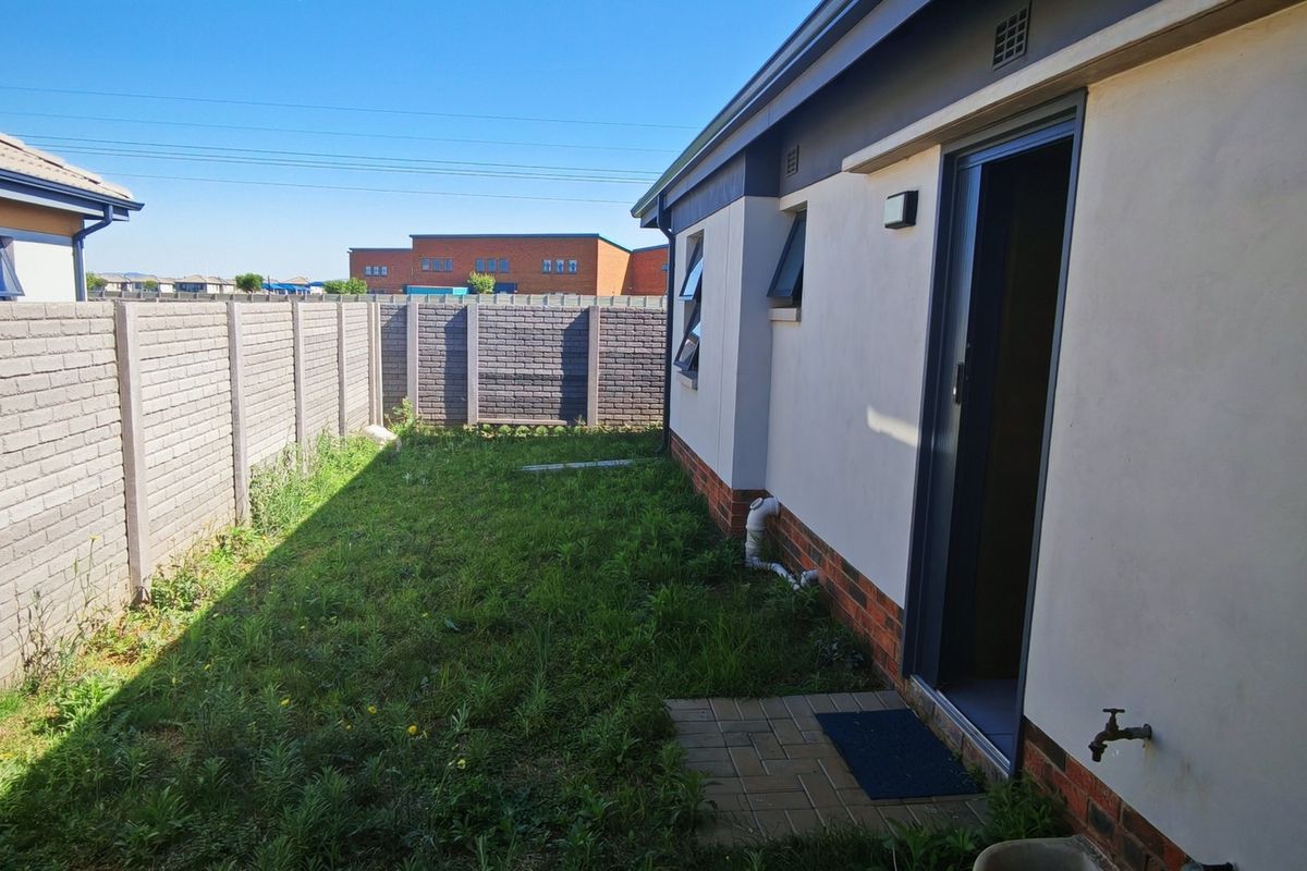 Rear exterior view of the property featuring a private garden area enclosed by a precast concrete boundary wall and a paved walkway.