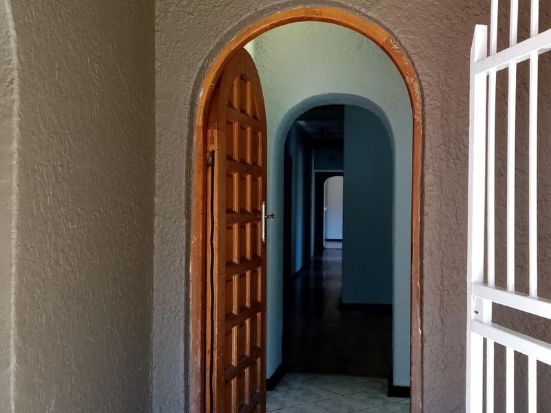 An arched entryway featuring a classic wooden panelled door, tiled flooring, and a security gate, leading into a hallway with additional arched transitions.
