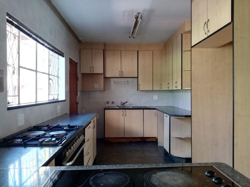 A functional kitchen featuring built-in cabinetry, gas stove, electric hob, and tiled flooring, offering a practical layout with ample storage space.