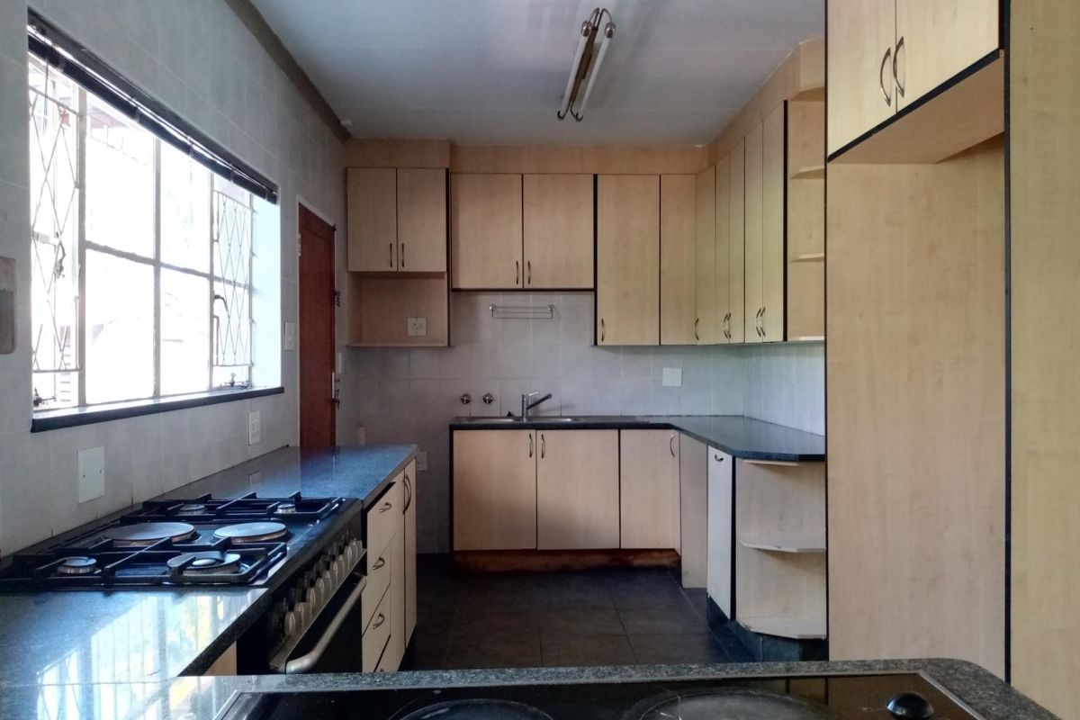 A functional kitchen featuring built-in cabinetry, gas stove, electric hob, and tiled flooring, offering a practical layout with ample storage space.