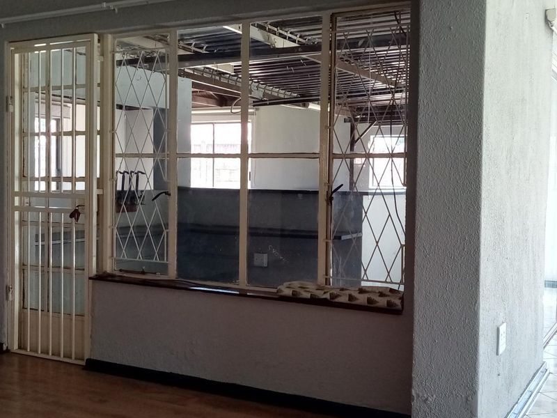 An empty living area featuring laminate flooring, a security gate, and an exposed ceiling structure, offering a blank canvas for renovation.