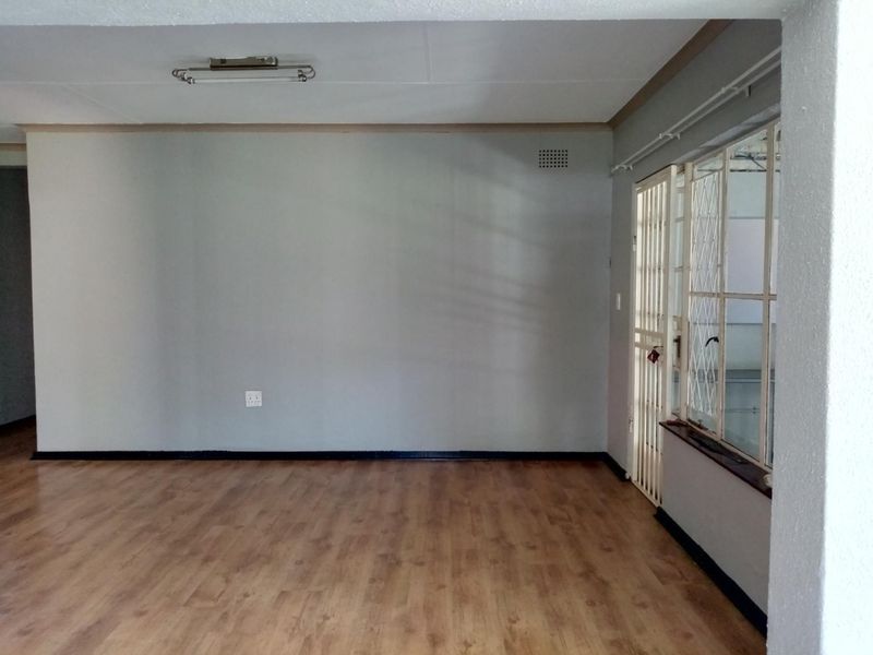 An empty living room featuring laminate flooring, a security gate, and steel window frames, offering a blank canvas for interior design.