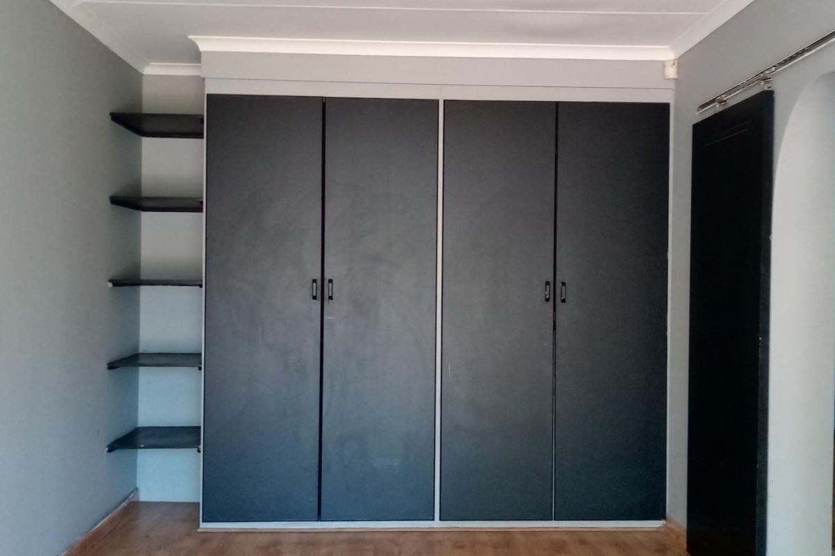 A bedroom featuring dark built-in cupboards with integrated open shelving, laminate flooring, and a decorative archway leading to an adjacent space.