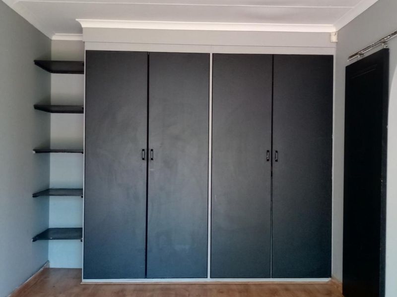 A bedroom featuring dark built-in cupboards with integrated open shelving, laminate flooring, and a decorative archway leading to an adjacent space.