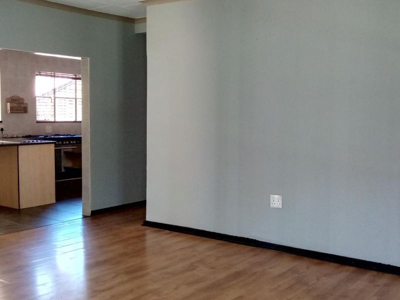 An open-plan living area featuring laminate flooring, leading into a functional kitchen space with built-in cabinetry and stove.