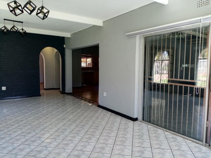 Spacious living area featuring tiled flooring, an elegant archway, exposed brick feature wall, and large sliding glass doors leading to the exterior.