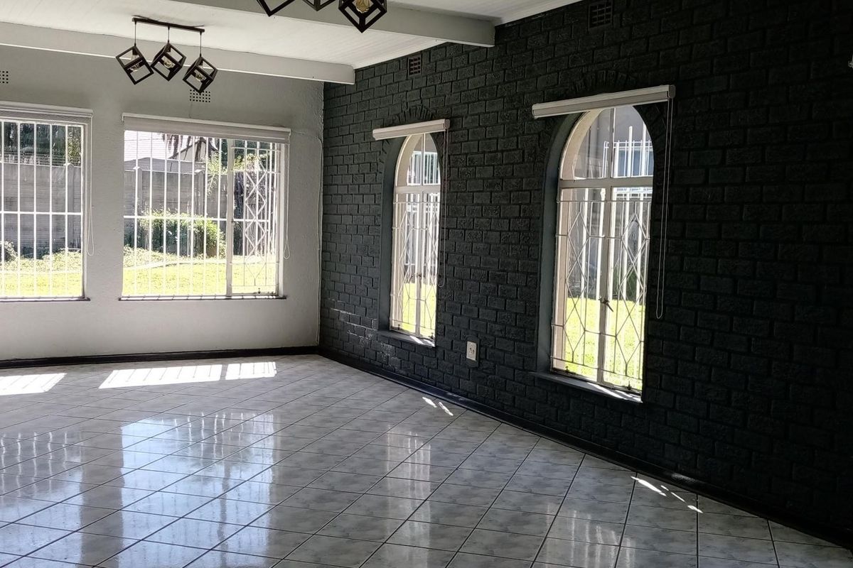 Spacious living area featuring polished tile flooring, a striking dark exposed brick feature wall, and large arched windows with security bars.