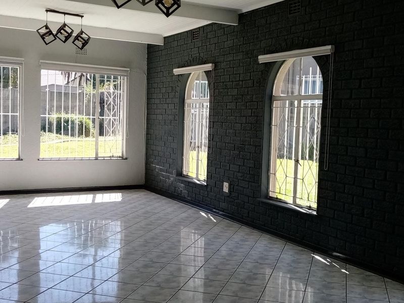 Spacious living area featuring polished tile flooring, a striking dark exposed brick feature wall, and large arched windows with security bars.