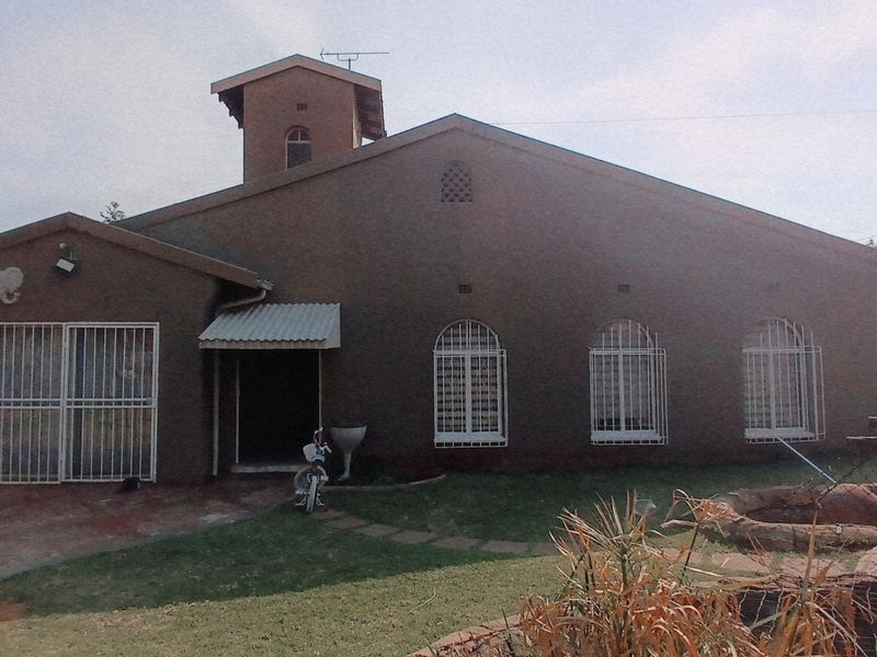 Front elevation of a single-story house featuring a distinctive tower, security bars on windows, and a paved driveway entrance.