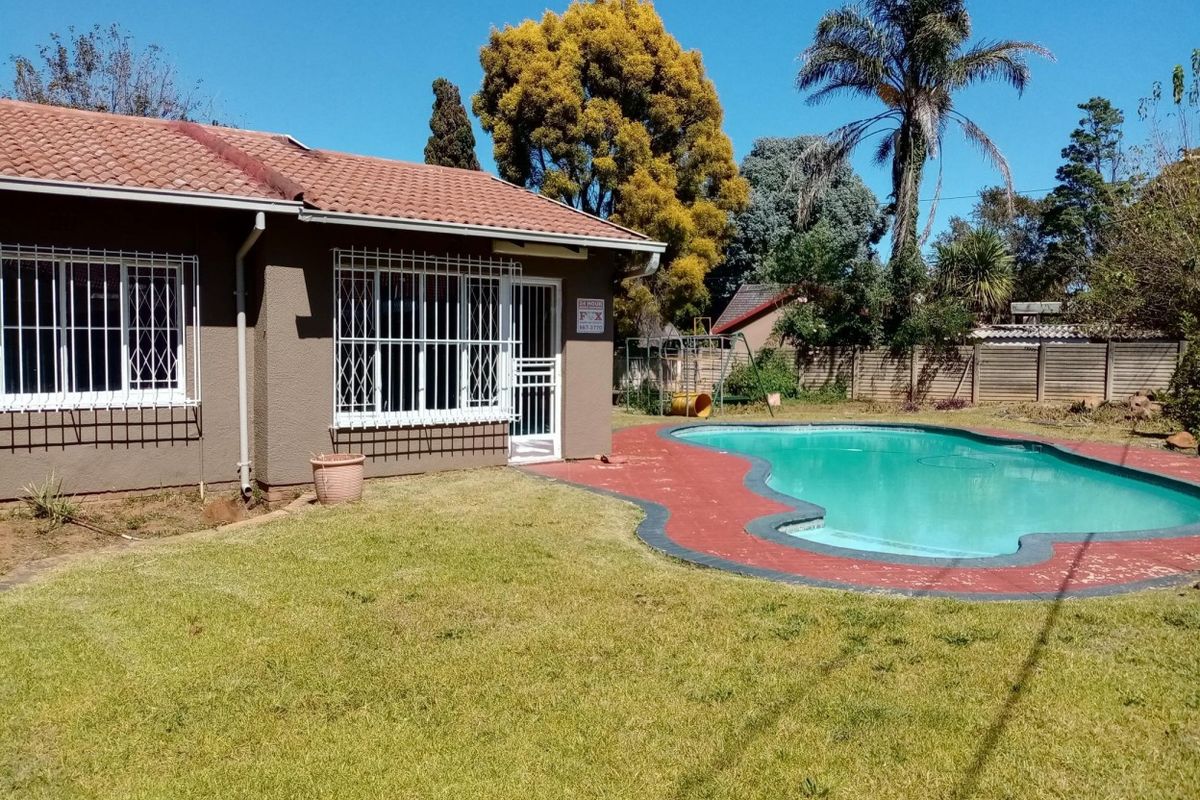 Rear exterior view of the house featuring a swimming pool, lawn area, and security features on windows and doors.