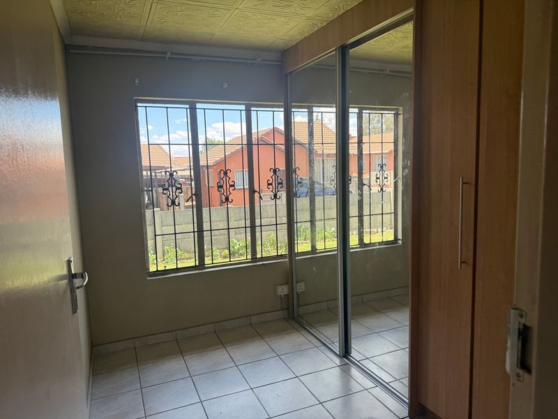 A vacant bedroom featuring tiled flooring, built-in cupboards with mirrored sliding doors, and security bars on the windows.