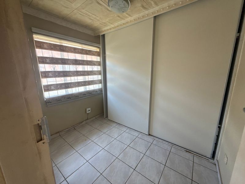 An empty bedroom featuring tiled flooring, a built-in sliding door wardrobe, and a window with security bars and blinds.