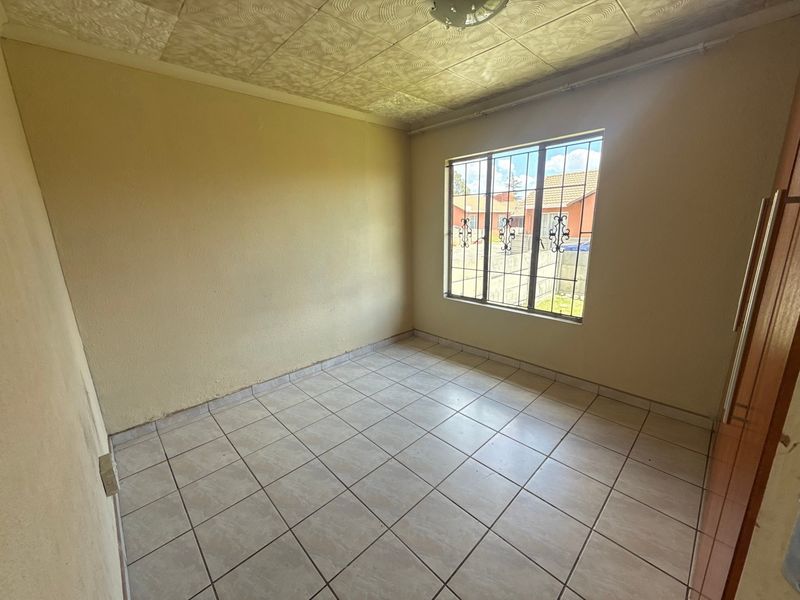 An empty bedroom featuring tiled flooring, security bars on the window, and built-in cupboard storage.