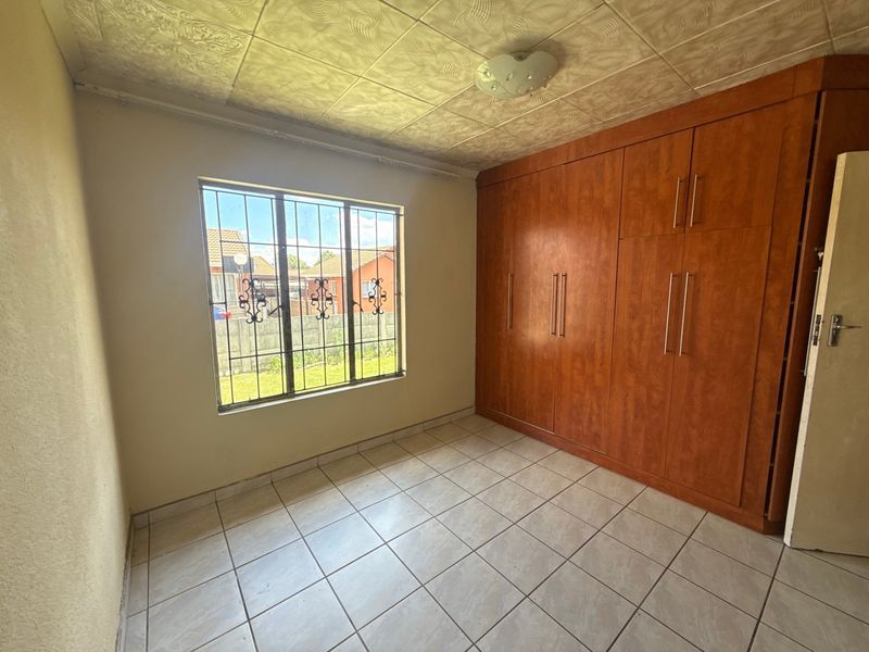 A vacant bedroom featuring tiled flooring, built-in wooden cupboards, and security bars on the window.