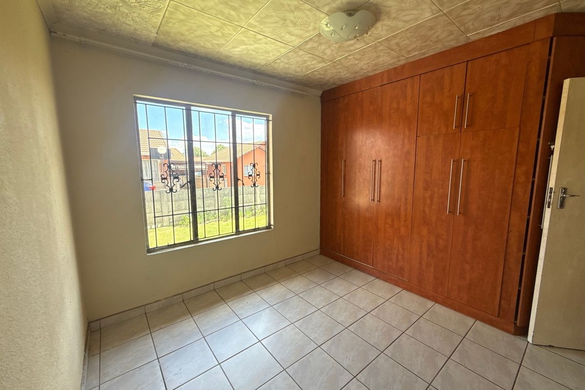 A vacant bedroom featuring tiled flooring, built-in wooden cupboards, and security bars on the window.
