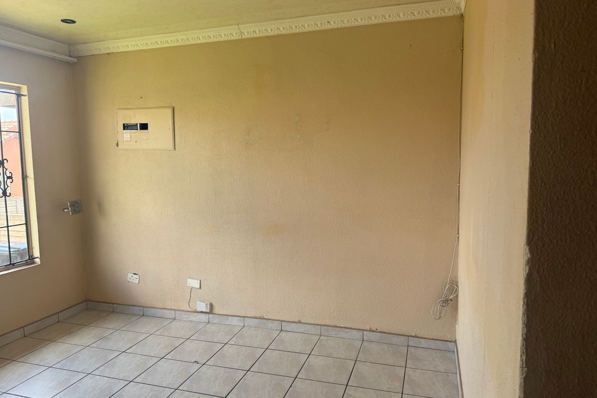 An empty living area featuring ceramic floor tiles, recessed lighting, and decorative coving, requiring cosmetic updates to the wall finishes.